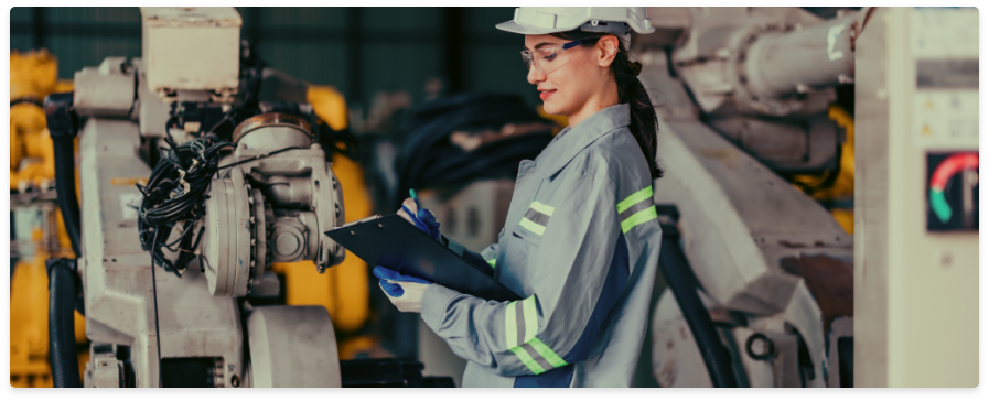 Technicienne équipée d’un casque de sécurité utilisant une tablette devant une machine industrielle en atelier
