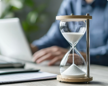 Sablier posé sur un bureau devant un ordinateur portable, illustrant la gestion du temps